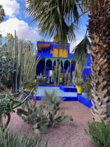 Bright blue architectural structure surrounded by cacti and palm trees in a desert-themed garden.